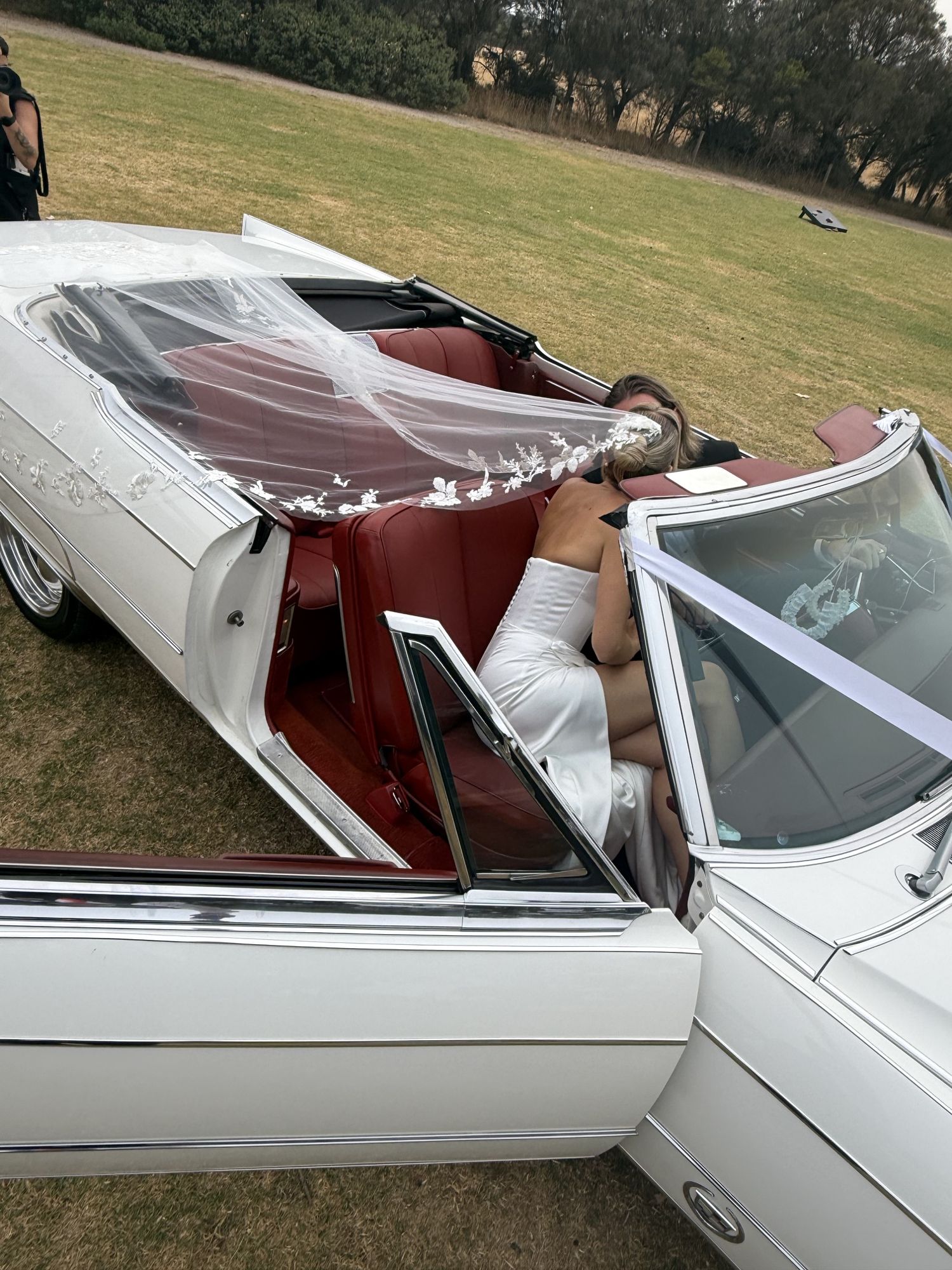 Bride stepping out of Queen B, Caddyman's white 1966 Cadillac Coupe De Ville convertible, with the door open