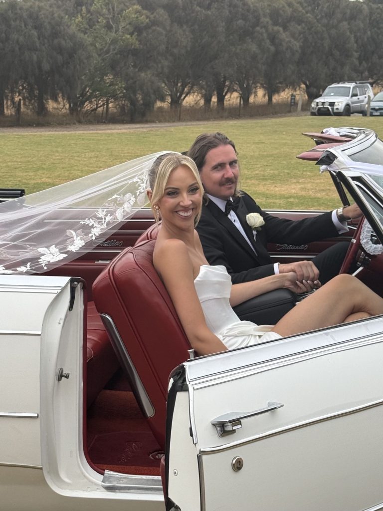 Bride and groom seated in Queen B, Caddyman's white 1966 Cadillac Coupe De Ville convertible, in open Melbourne parkland