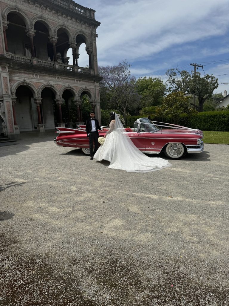 Bride and groom beside Rosie, Caddyman's 1959 Rose Pink Pearl Cadillac convertible, outside a historic Melbourne mansion