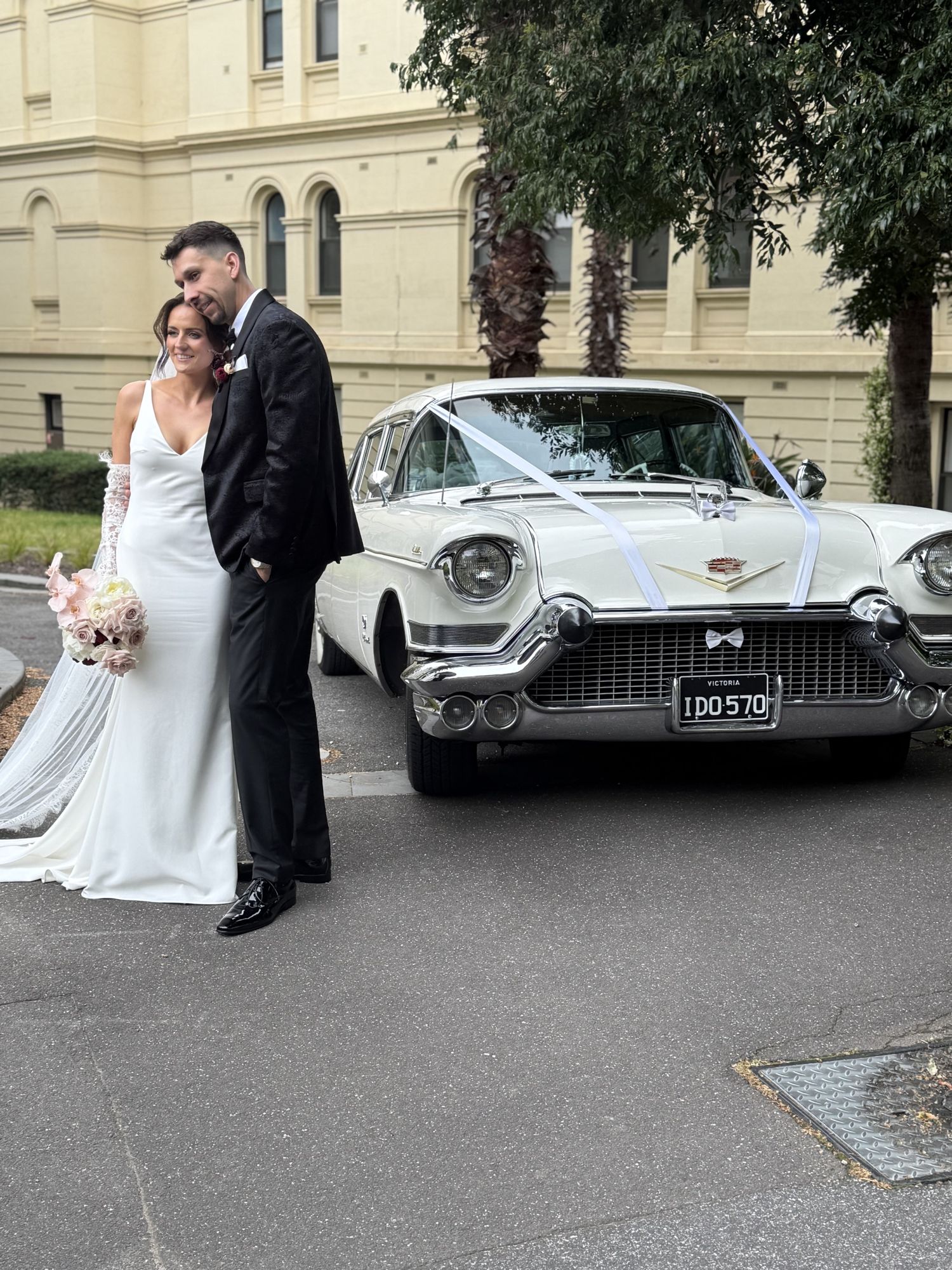 Bride and groom in front of The Duchess, Caddyman's white 1957 Cadillac Series 75 wedding limousine, showing the chrome grille