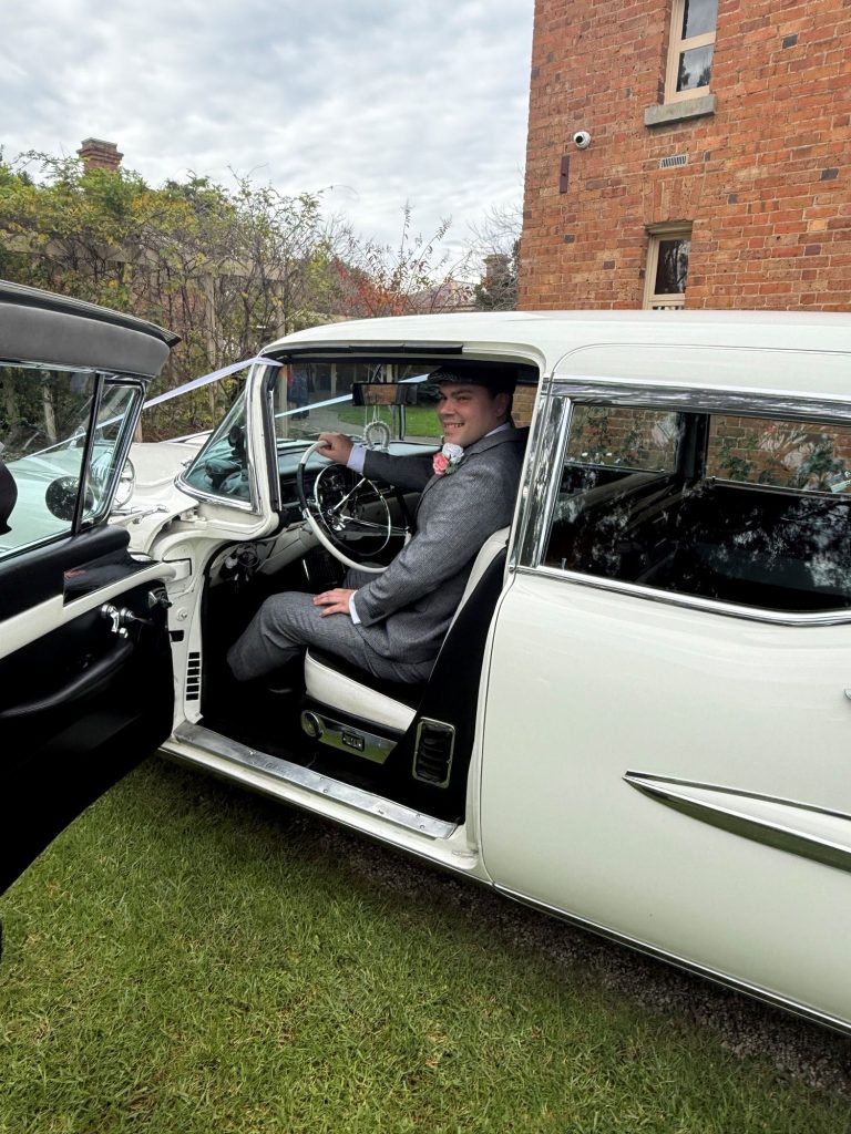 Groom at the open rear door of The Duchess, Caddyman's white 1957 Cadillac Series 75 wedding limousine