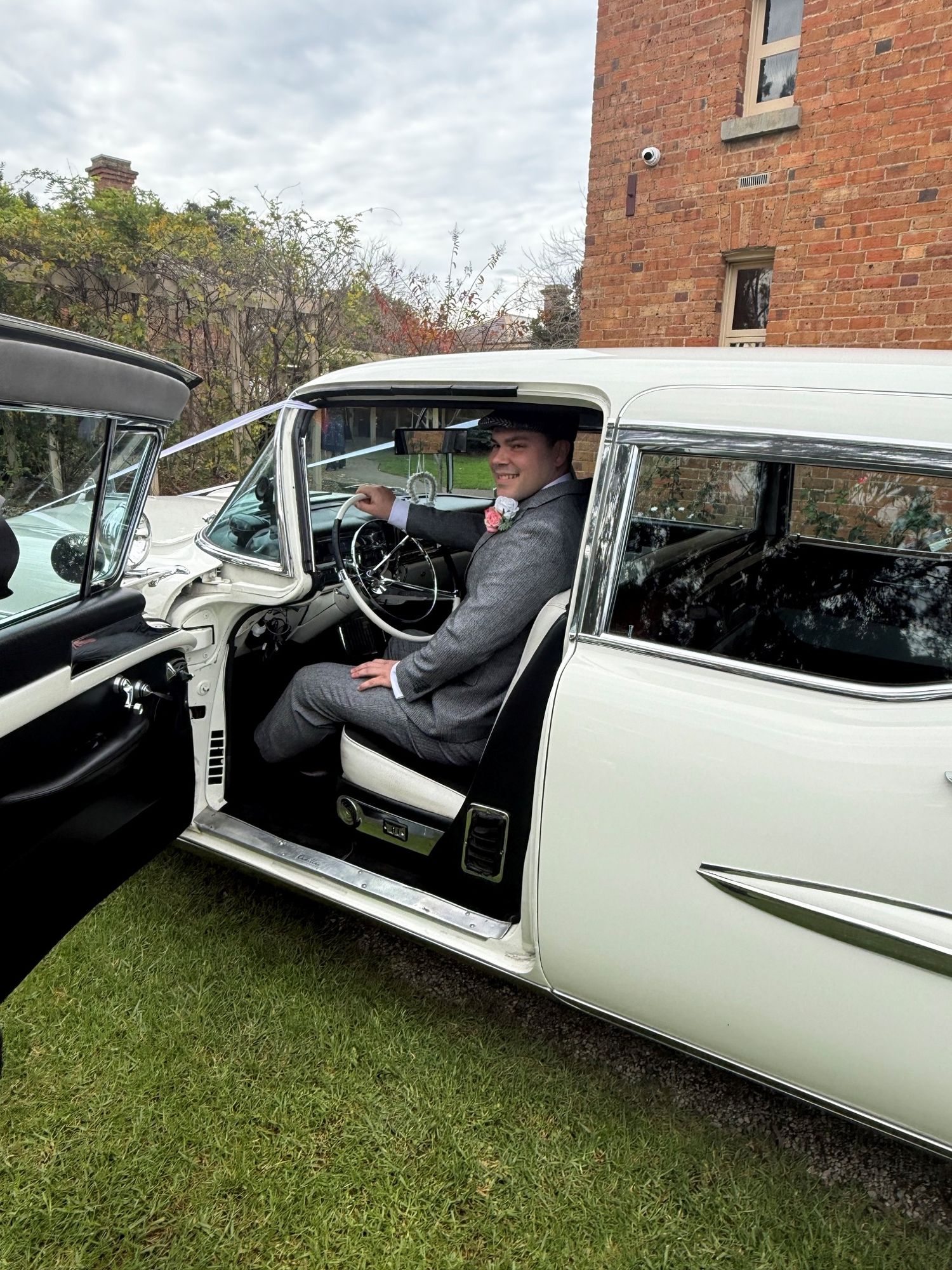 Groom at the open rear door of The Duchess, Caddyman's white 1957 Cadillac Series 75 wedding limousine