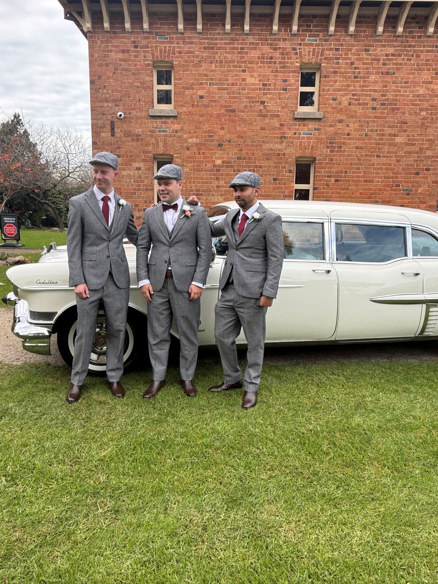 Three groomsmen standing beside The Duchess, Caddyman's white 1957 Cadillac Series 75 wedding limousine