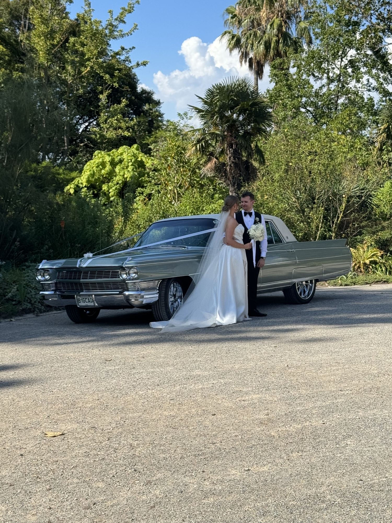 Bride and groom beside The Pres, Caddyman's classic Cadillac Fleetwood sedan, in a garden setting