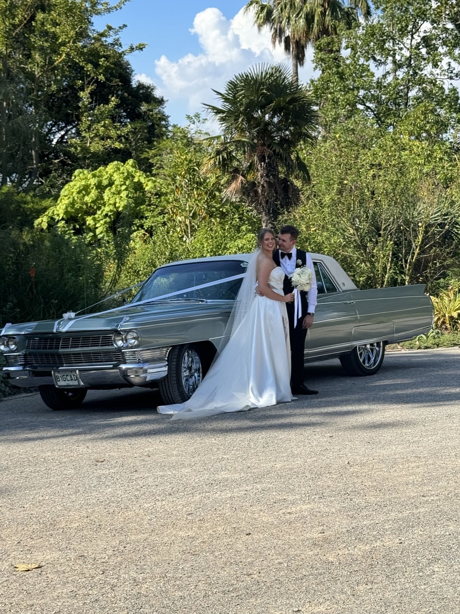 Bride and groom with The Pres, Caddyman's classic Cadillac Fleetwood sedan, side view with wedding ribbons