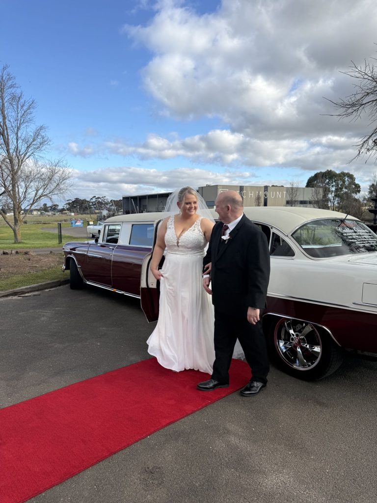 Bride and groom on the red carpet beside The Prince of Belair, Caddyman's maroon 1955 Chevrolet Bel Air stretch limousine