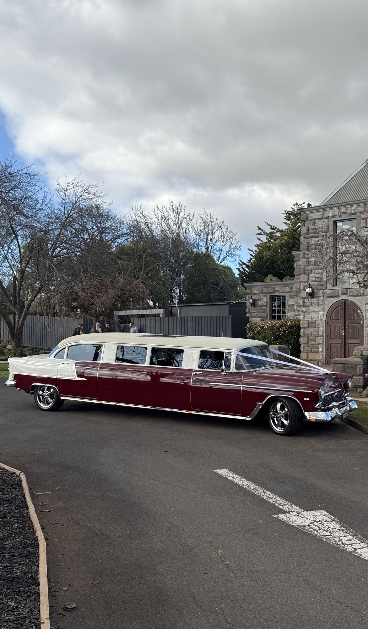 Side view of The Prince of Belair, Caddyman's maroon 1955 Chevrolet Bel Air stretch limousine outside a stone church